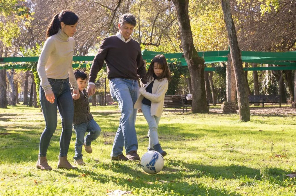 A family plays soccer together in a sunny park, enjoying quality time outdoors.
